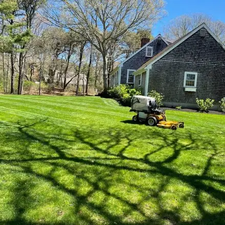 Mower cutting a lawn beside a Cape Cod home