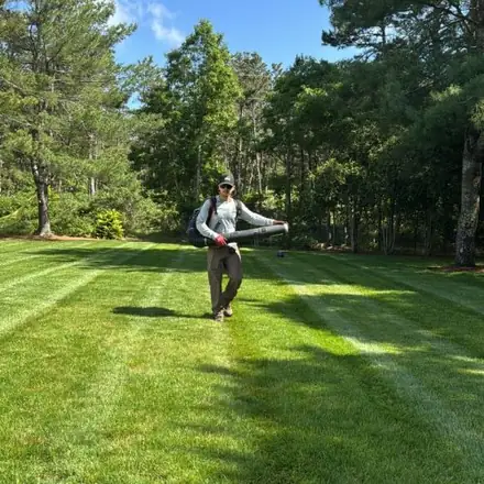 Crew member blowing leaves on a striped lawn