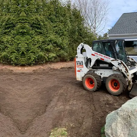 Bobcat skid steer grading a yard beside a boulder